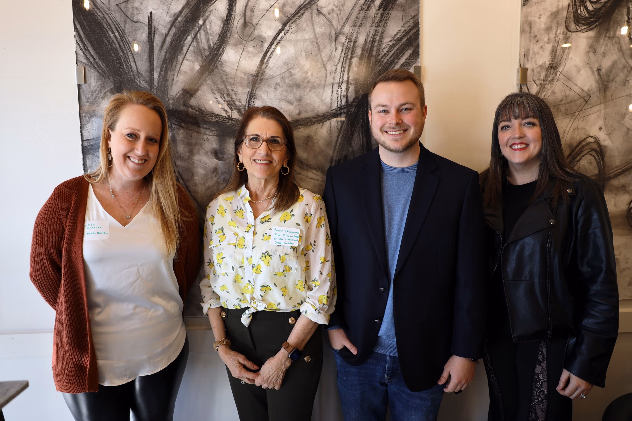 Group of four professionals posing together, highlighting community engagement and collaboration in virginia, with a backdrop of abstract art, representing TechArk's focus on advancing AI initiatives.